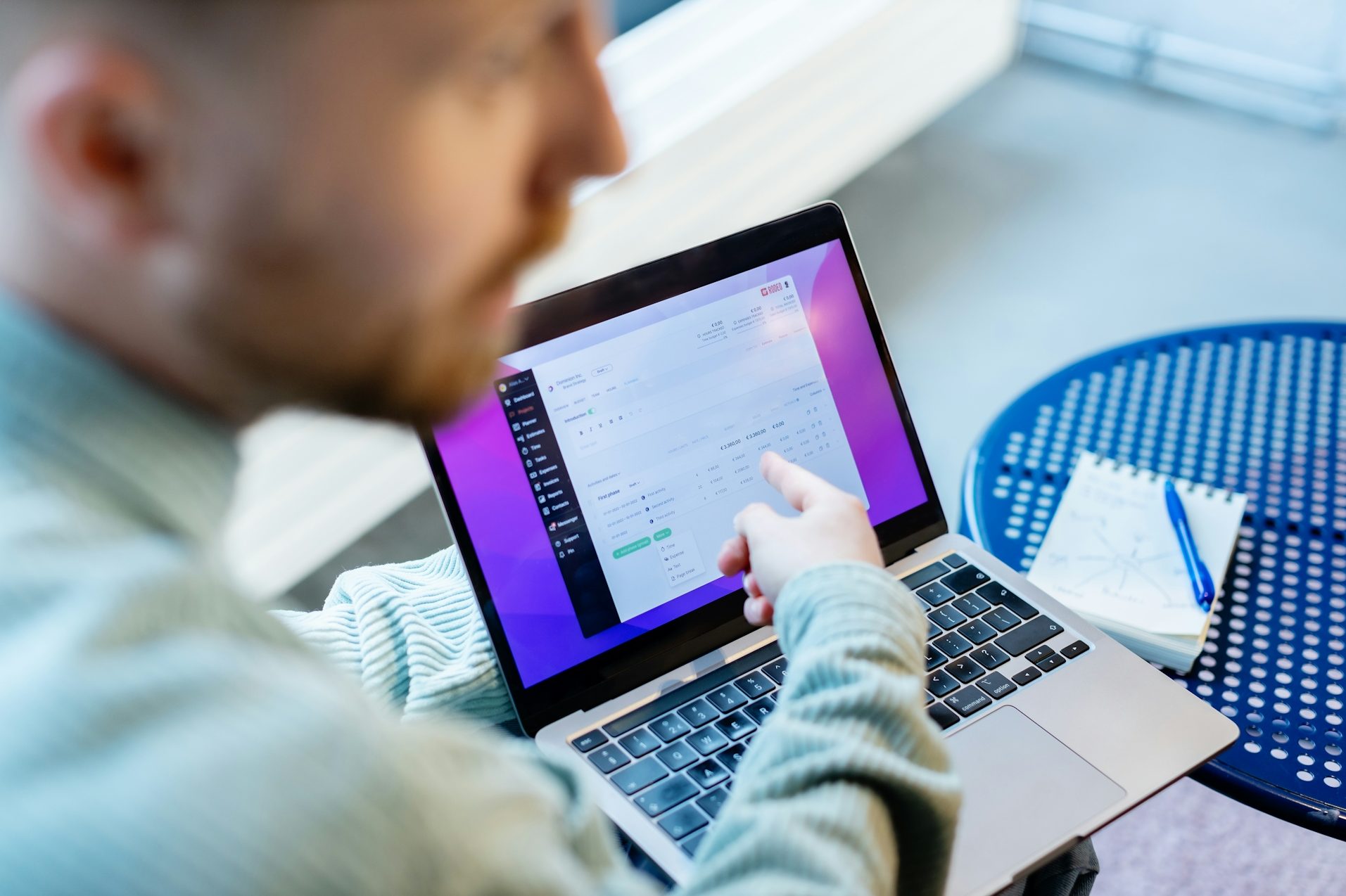 A person points at a laptop screen while sitting at a table.