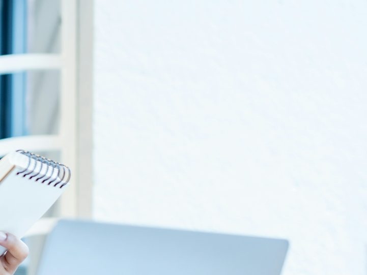 A person holding a notepad beside a laptop in a bright, modern setting.